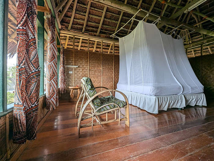 Cabin at Ambua Lodge furnished with a chair and mosquito netting over bed